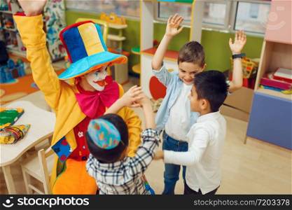 Funny clown with cheerful children play counting game together. Birthday party celebrating in playroom, baby holiday in playground. Childhood happiness, childish leisure. Clown with cheerful children play counting game
