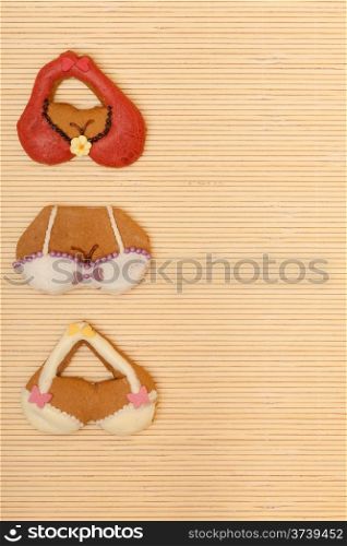 Funny colorfull bikini bra shape gingerbread cakes cookies sweet dessert with icing and decoration border or frame on beige bamboo mat background