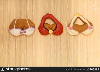 Funny colorfull bikini bra shape gingerbread cakes cookies sweet dessert with icing and decoration border or frame on beige bamboo mat background