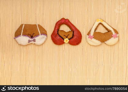 Funny colorfull bikini bra shape gingerbread cakes cookies sweet dessert with icing and decoration border or frame on beige bamboo mat background