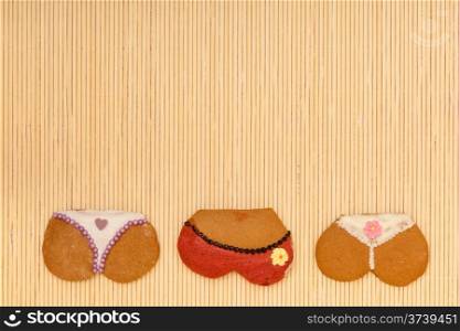 Funny colorfull bikini female panties shape gingerbread cakes cookies sweet dessert with icing and decoration border or frame on beige bamboo mat background