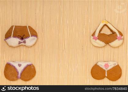 Funny colorfull bikini shape gingerbread cakes cookies sweet dessert with icing and decoration border or frame on beige bamboo mat background