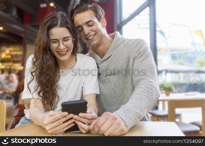 Funny couple or marriage sharing a smart phone to watch media content sitting in a restaurant