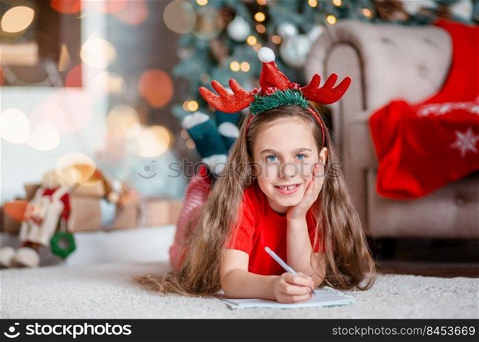 Funny cute caucasian girl writes a letter to Santa Claus near the Christmas tree. Happy childhood, time of miracles and desires. Merry Christmas.. Funny cute caucasian girl writes a letter to Santa Claus near the Christmas tree. Happy childhood, time of miracles and desires.