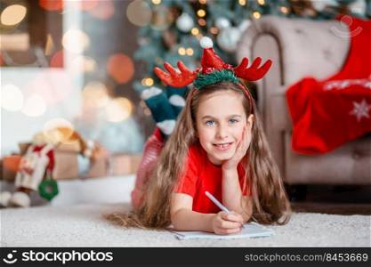 Funny cute caucasian girl writes a letter to Santa Claus near the Christmas tree. Happy childhood, time of miracles and desires. Merry Christmas.. Funny cute caucasian girl writes a letter to Santa Claus near the Christmas tree. Happy childhood, time of miracles and desires.