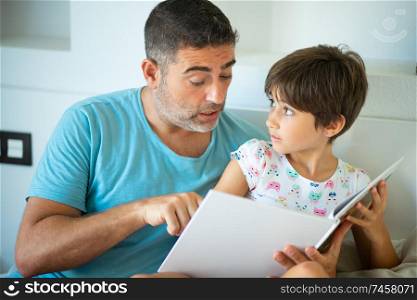 Funny dad and lovely little girl are having fun on the bed. Middle-age father with her eight years daughter using digital tablet in bedroom.. Middle-age father with her eight years daughter using digital tablet in bedroom.