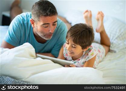Funny dad and lovely little girl are having fun on the bed. Middle-age father with her eight years daughter using digital tablet in bedroom.. Middle-age father with her eight years daughter using digital tablet in bedroom.