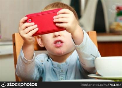 Funny dirty boy child kid taking photo with red mobile phone indoor. At home. Technology generation.