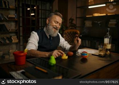 Funny elegant older businessman smoking cigar and playing toys at work table in home office. Funny elegant older businessman smoking cigar and playing toys at work table