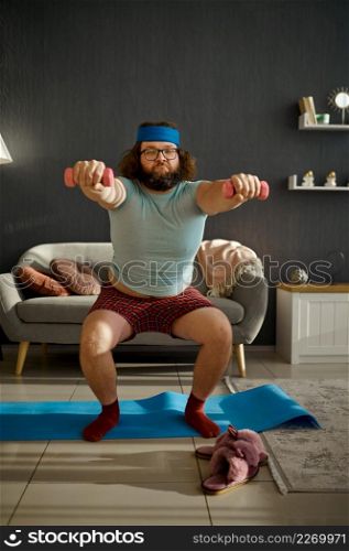 Funny fat man does morning workout with dumbbells at home. Sports, healthy lifestyle and weight loss. Funny man doing morning workout with dumbbells