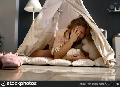 Funny freelance businessman touching sleepy face awake in teepee tent. Morning at home office. Funny freelance businessman awake in teepee tent