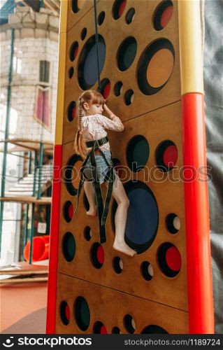 Funny girl climbing walls in children game center. Excited child having fun on playground indoors. Female kid playing in amusement centre, activity attraction. Funny girl climbing walls in children game center