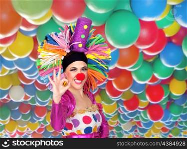Funny girl clown with a big colorful wig saying Ok with many ballons of background