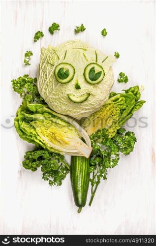 funny girl face made of green vegetables, cucumber and lettuce on white wooden background
