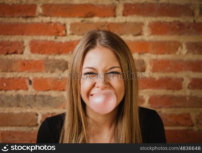 Funny girl making a pomp with a bubble gum and a brick wall of background