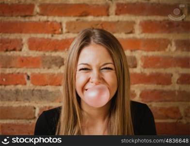 Funny girl making a pomp with a bubble gum and a brick wall of background