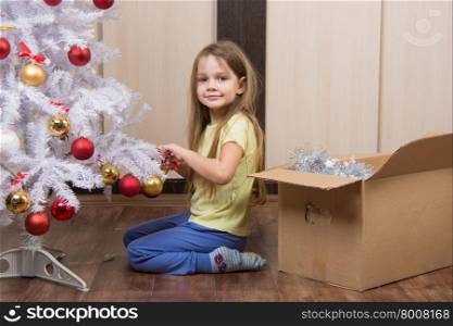 Funny girl takes off a Christmas tree with toys. five year old girl takes fun toys with artificial Christmas tree