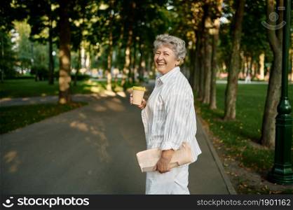 Funny granny drinks coffee in summer park. Aged people lifestyle. Pretty grandmother having fun outdoors, old female person on nature. Funny granny drinks coffee in summer park