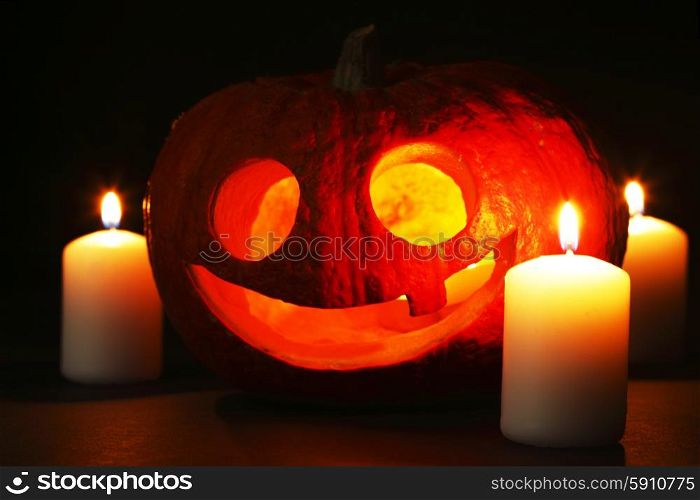 Funny Halloween pumpkin and burning candles on black background