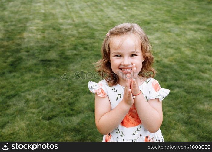 Funny happy little girl laughs on a background of green grass. Childhood concept, ready for your text, logo or symbols. Funny happy little girl laughs on a background of green grass. Childhood concept, ready for your text, logo or symbols.