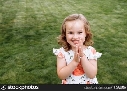 Funny happy little girl laughs on a background of green grass. Childhood concept, ready for your text, logo or symbols. Funny happy little girl laughs on a background of green grass. Childhood concept, ready for your text, logo or symbols.