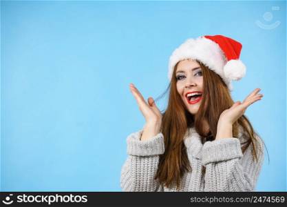 Funny happy surprised, young woman wearing Santa Claus red hat having fun. Pretty lady is ready for Christmas Holiday season. Blue background.. Funny surprised woman in Christmas Santa hat