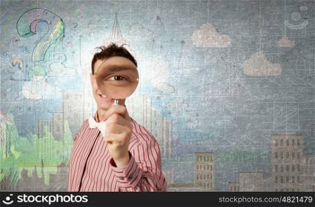 Funny image of young man looking in magnifying glass. Guy looking in magnifying glass