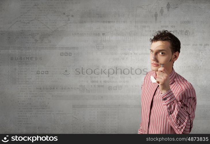 Funny image of young man looking in magnifying glass. Guy looking in magnifying glass