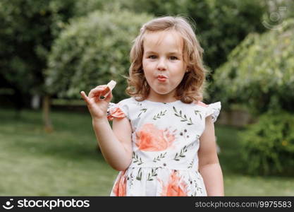 Funny kid girl eating sandwich outdoors. Having fun. Looking at camera. Posing over nature background. Healthy food. Childhood. Funny kid girl eating sandwich outdoors. Having fun. Looking at camera. Posing over nature background. Healthy food. Childhood.