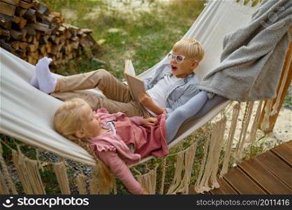Funny kids lying in a hammock, summer camping. Family with children travel in camp car, nature and forest on background. Campsite adventure, travelling lifestyle. Funny kids lying in a hammock, summer camping