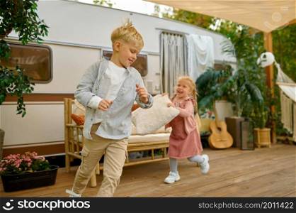 Funny kids play at the trailer, summer camping. Family with children travel in camp car, nature and forest on background. Campsite adventure, travelling concept. Funny kids play at the trailer, summer camping