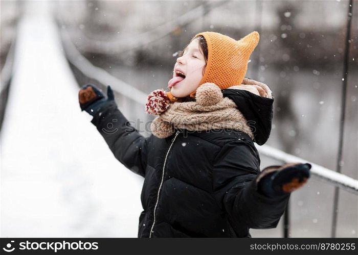 Funny little girl catches snowflakes in a beautiful winter park during a snowfall. Cute baby is playing in the snow. Winter activities for children. the winter holidays. happy childhood. Funny little girl catches snowflakes in a beautiful winter park during a snowfall. Cute baby is playing in the snow. Winter activities for children. the winter holidays. happy childhood.