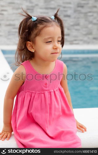 Funny little girl with pigtails sitting near the pool