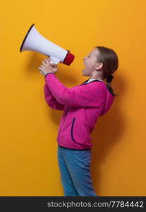 Funny little kid girl Screaming in megaphone over the yellow background in studio. People sincere emotions lifestyle concept. Mock up copy space. High quality photo. Funny little kid girl Screaming in megaphone over the yellow background in studio. People sincere emotions lifestyle concept.