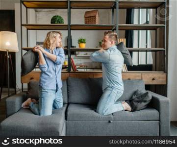 Funny love couple staged fights on the pillows. Husband and wife having fun in living room. Happy playful family resting together