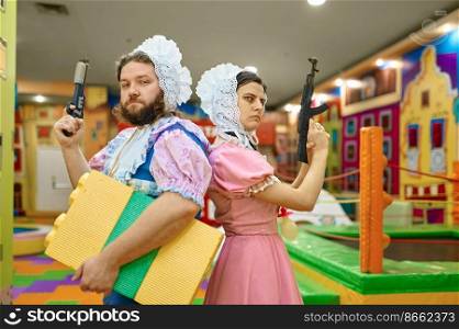 Funny man and woman like baby gangsters with guns standing over playroom interior. Man and woman like baby gangsters with guns