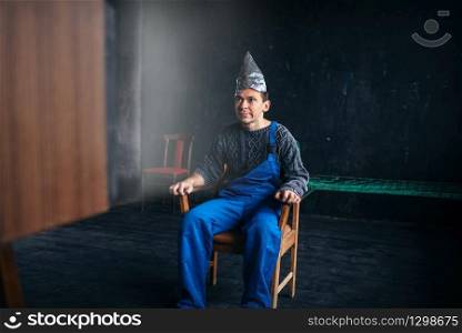Funny man in tinfoil hat sits in chair, paranoia concept. UFO, conspiracy theory, brain theft protection, phobia