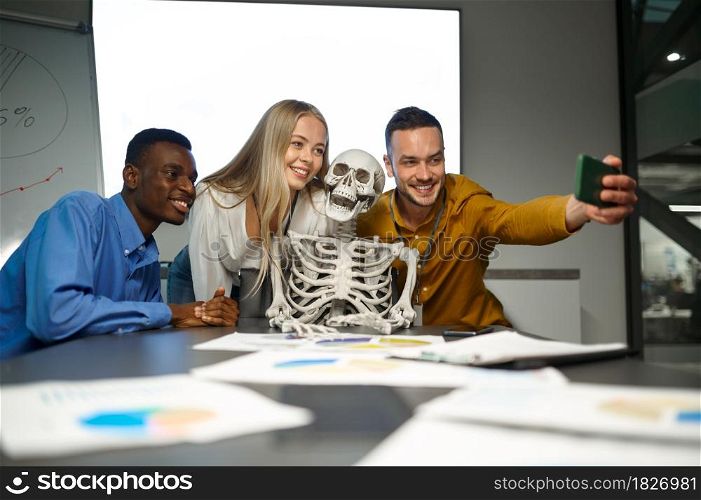 Funny managers, selfie with skeleton, conference in IT office, joke. Professional teamwork and planning, group brainstorming and corporate work, meeting of colleagues. Funny managers, selfie with skeleton in IT office