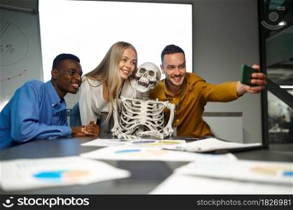 Funny managers, selfie with skeleton, conference in IT office, joke. Professional teamwork and planning, group brainstorming and corporate work, meeting of colleagues. Funny managers, selfie with skeleton in IT office