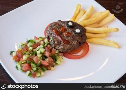 Funny meat cutlet face. Funny meat cutlet face with french fries as hair and cutted vegetables for children menu