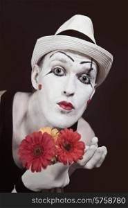 Funny mime in white hat with bouquet of red gerberas on black background