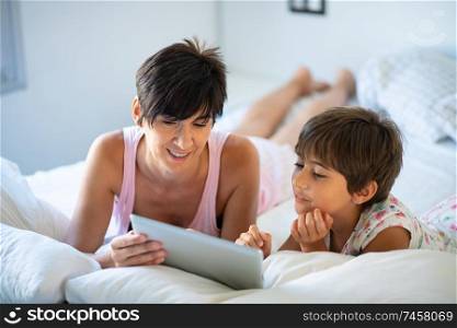 Funny mom and lovely little girl are having fun on the bed. Middle-age mother with her eight years daughter using digital tablet in bedroom.. Middle-age mother with her eight years daughter using digital tablet in bedroom.