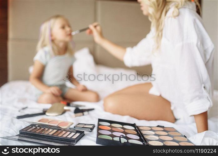 Funny mother and child plays with makeup on the bed at home. Parent feeling, togetherness, happy times. Funny mother and child plays with makeup on bed