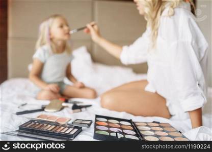 Funny mother and child plays with makeup on the bed at home. Parent feeling, togetherness, happy times. Funny mother and child plays with makeup on bed