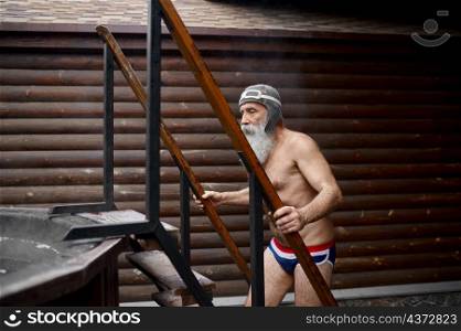 Funny old senior man climbing stairs to wooden outside sauna bathtub. Spa resort and thermal bath. Senior man climbing stairs to outside bathtub