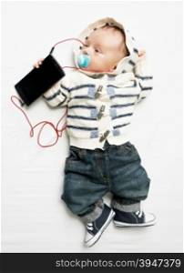 Funny photo of cute baby boy listening to music on phone with earphones