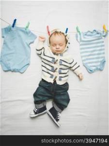 Funny photo of little baby boy in jeans hanging on cord next to drying clothes