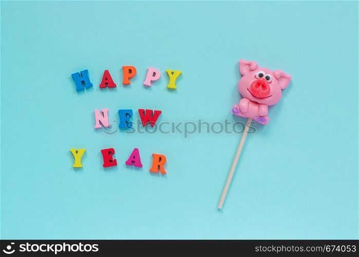 Funny pink pig lollipop and multicolor inscription Happy New Year on blue background. Top view Layout Concept greeting card Year of the pig.. pig lollipop and text Happy New Year
