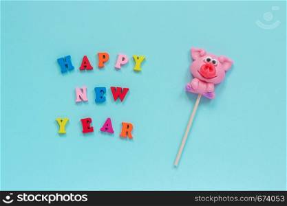 Funny pink pig lollipop and multicolor inscription Happy New Year on blue background. Top view Layout Concept greeting card Year of the pig.. pig lollipop and text Happy New Year