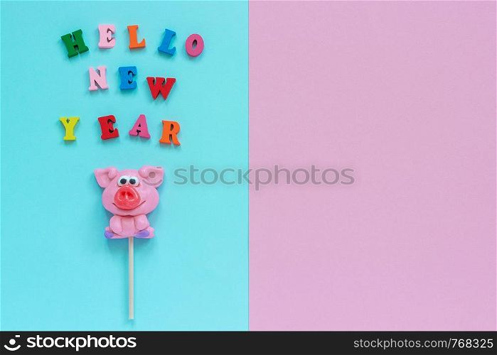 Funny pink pig lollipop and multicolor inscription Hello New Year on blue pink background. Top view Copy space Layout Concept greeting card Year of the pig.. pig lollipop and text Hello New Year